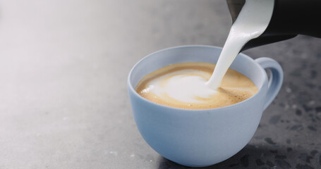 Pour steamed milk into espresso to make cappuccino in blue cup on concrete background