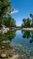 Obraz premium A crystal clear river reflecting lush green trees under a bright blue sky