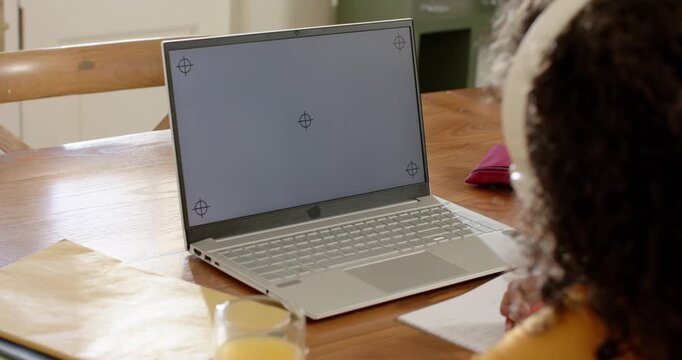 Picking up red pencil and leaning forward, student is writing notes while studying on silver laptop