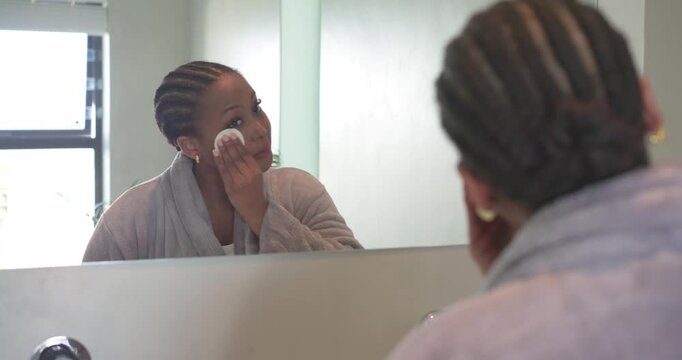 African American woman viewing mirror at bathroom sink grabbing pad wiping face for cleansing