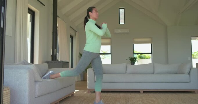 Mid-adult Asian woman entering living room doing Bulgarian split squats on sofa for fitness