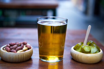 A glass of beer with snacks on a wooden table.