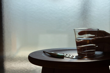 窓際に置かれた体温計と薬とコップに入った水