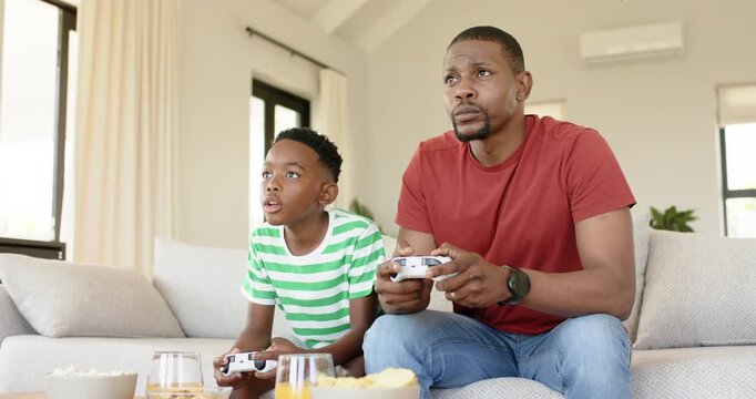 Black father and son gaming at home, celebrating game win raising controller while father guiding