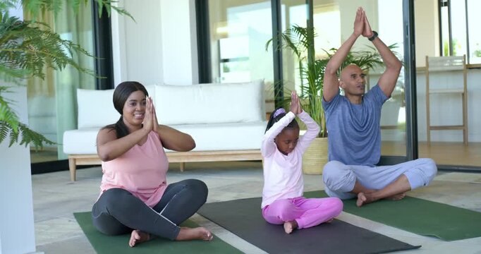 Diverse family following guided breathing and stretching sequence on yoga mats on patio meditating