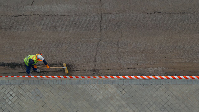Worker preparing road for paving, removing loose asphalt from damaged surface
