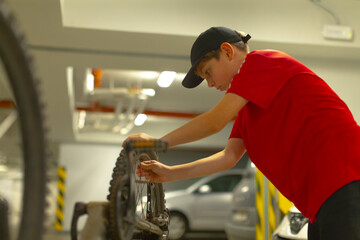 focused caucasian teen adjusting bike chain and sprocket under fluorescent light in underground parking garage, red shirt and cap, hands working with wrench, attention to detail, small toolkit