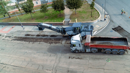 Heavy machinery processing old asphalt from a street into a dump truck