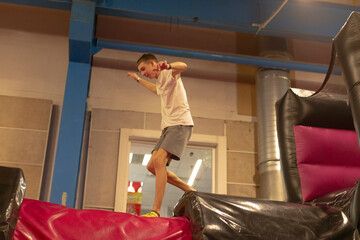 Teen boy balancing on inflatable obstacle showing playful confidence and dynamic motion in indoor softplay gym white shirt and shorts, arms outstretched for balance, vibrant cushions and padded