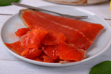 Cold smoked trout fillet sliced on a ceramic plate closeup on a white table. Fish delicacy