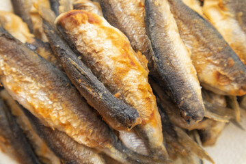 A close-up shot of a pile of small fried fish showcasing their golden-brown, crispy skin and oily sheen, perfect for a rustic seafood dish.