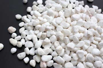 Smooth, white, polished pebbles scattered on a dark black surface.
