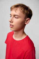 Boy in a red shirt, looking to the left with a thoughtful expression, clean studio backdrop, casual fashion and youth style, close cropped profile shot suitable for lifestyle, education, or creative