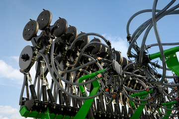 A large green seed drill folded against a cloudy sky.