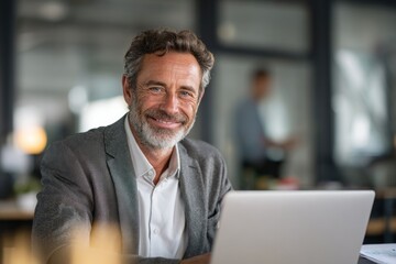 Smiling middle aged businessman sitting at desk with laptop computer