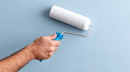 Hand of a male painter holding a paint roller, applying fresh paint on a smooth blue wall, showcasing the home improvement process and creativity in interior design