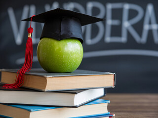 Green apple wearing a graduation cap sits atop stacked books with a chalkboard behind