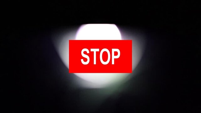 Un primer plano de un rect&aacute;ngulo de color rojo con la palabra detener y una luz blanca en movimiento en un fondo negro