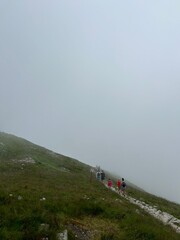 Group of hikers walking along a grassy mountain trail in dense fog. Hikers walking up foggy mountain trail.
