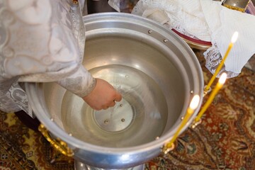 Priest hand touches consecrated water in baptismal font
