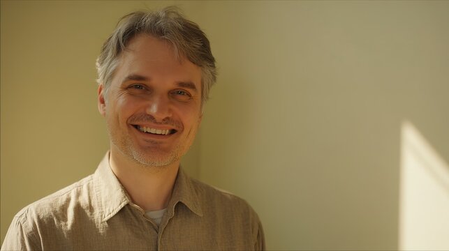 A middleaged man with graying hair smiles warmly in a casual shirt