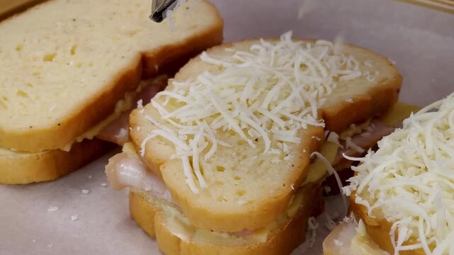 Grating mozzarella cheese on three delicious croque monsieur style sandwiches on baking sheet