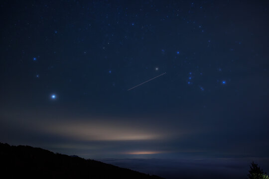vista panoramica del cielo notturno stellato e parzialmente sereno, a inizio inverno, da un'alta quota in montagna, nel nord Italia, con nuvole che coprono le valli