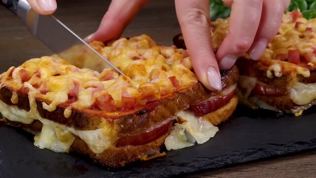 Close up of cutting a freshly baked croque monsieur style ham and cheese sandwich on slate