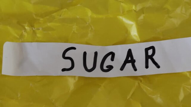 Un primer plano de un papel de color blanco con la palabra az&uacute;car en un fondo amarillo en movimiento