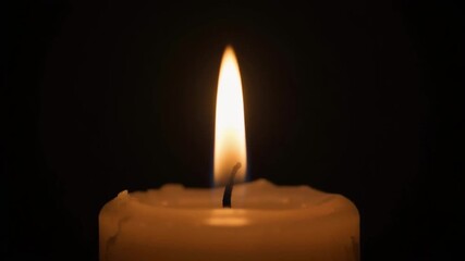 Close-up of a single burning candle flame in the dark symbolizing hope spirituality remembrance and tranquility.