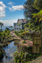 A serene garden scene in Madeira Monte Palace tropical garden in Funchal with lush greenery, a tranquil stream, and traditional architecture in the background. Ideal for nature lovers and tourists.