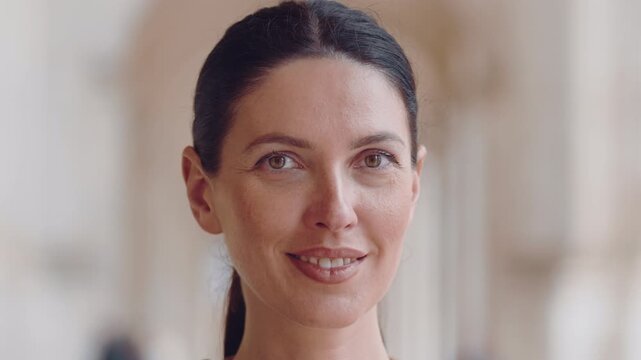 Closeup portrait of smiling woman with natural makeup and tied hair standing in bright corridor showing calm expression and confidence with blurred background