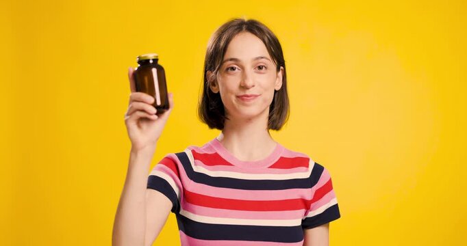 Young woman showcasing an empty brown pill bottle on a yellow background, displaying contentment