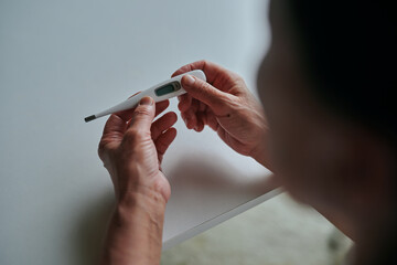 体温計で熱を測るシニア女性