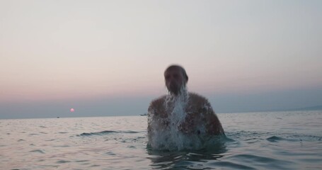 Man energetically splashing water in the sea at sunset, a serene evening scene
