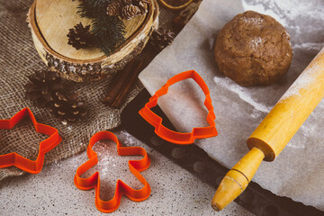 Rolled ginger dough on parchment paper, On the wooden surface there are metal gingerbread molds and a rolling pin.