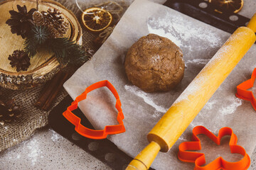 Rolled ginger dough on parchment paper, On the wooden surface there are metal gingerbread molds and a rolling pin.