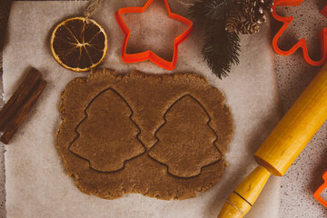 Rolled ginger dough on parchment paper, On the wooden surface there are metal gingerbread molds and a rolling pin.
