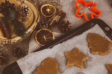 Tree and other shapes cut out from raw pastry dough on a sheet of baking paper - making homemade gingerbread Christmas cookies