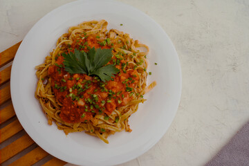 flat lay of a plate of spaghetti topped with tomato sauce mixed with meat, cheese, spices, onions and lettuce leaves stands on a wooden tray.