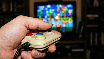 Mans hand holding retro video game controller while playing colorful game on old television. 90s nostalgia gaming concept. Vintage home entertainment and arcade fun during christmas season.