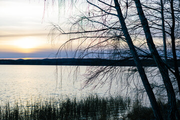Serene sunset over tranquil lake, with gentle ripples reflecting warm hues of orange and purple, surrounded by distant hills and soft clouds, creating a peaceful natural landscape