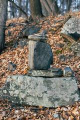 Stacked stones create a natural sculpture in a serene forest setting, surrounded by fallen leaves and trees, showcasing the beauty of nature and tranquility in the wilderness