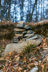 Stacked stones create a natural sculpture in a serene forest setting, surrounded by fallen leaves and trees, showcasing the beauty of nature and tranquility in the wilderness