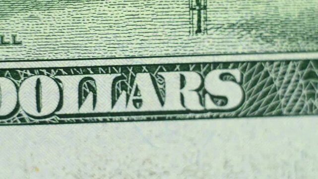 A green-toned close-up of a hundred-dollar bill fragment reveals fine engraved details as the camera shifts slightly across frames showing texture transitions and subtle horizontal movement.