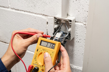 Close-up on an hands of electrician fixing an electrical outlet and measuring the voltage at a storage room - improvement concepts