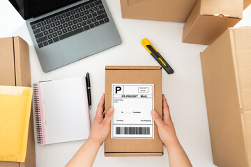 Above table top view of female warehouse worker or seller packing ecommerce shipping order box for dispatching, preparing post courier delivery package, dropshipping shipment service concept.
