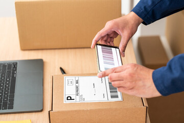 Fulfilling orders for her online store, this female dropshipper scans a barcode with his mobile phone, showcasing his entrepreneurship skills and dedication to customer satisfaction.