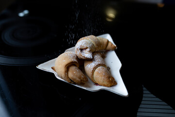 Close-up view of croissants being sprinkled with powdered sugar. Falling sugar highlights the fresh pastry texture in a simple bakery scene