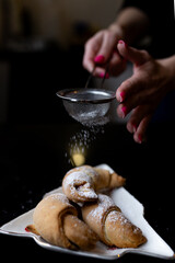 Close-up view of croissants being sprinkled with powdered sugar. Falling sugar highlights the fresh...